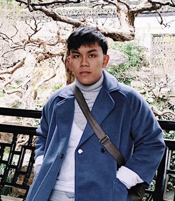 Person wearing blue jacket over white sweater and a satchel