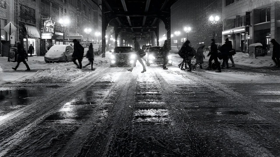 People walking in a city at night while its snowing.
