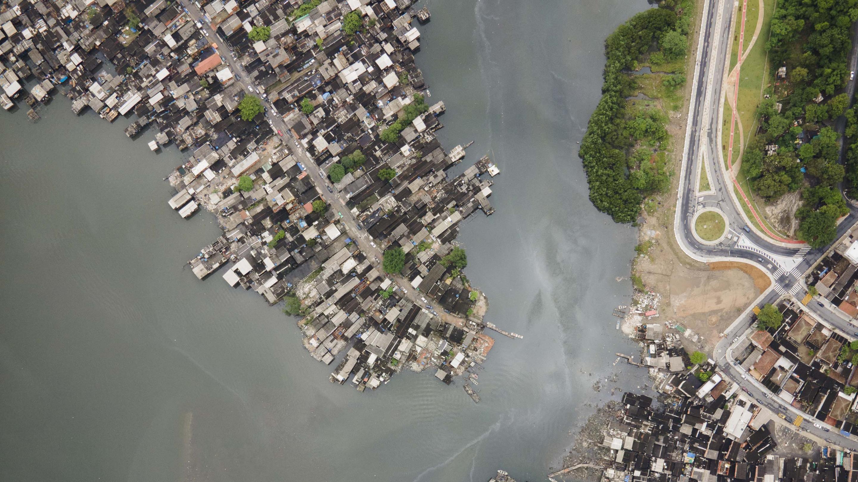 A body of water next to sheet metal houses next to large buildings surrounded by trees.