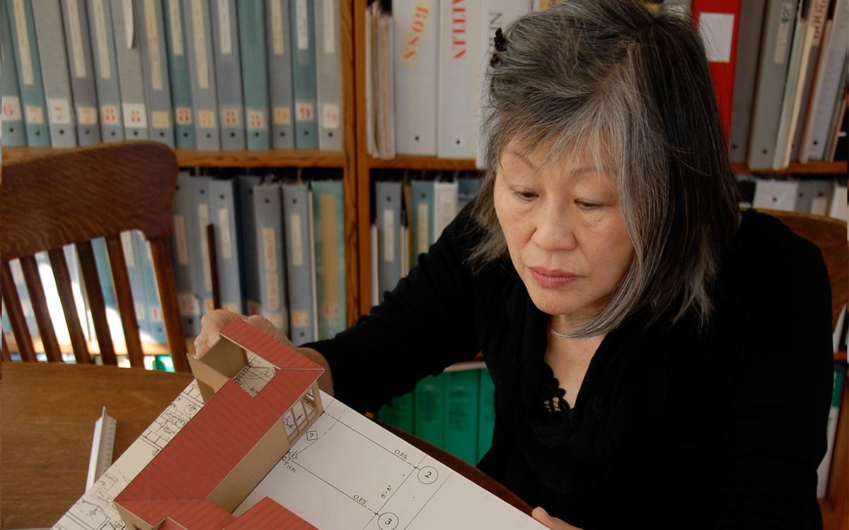 A person holding an architectural model and sitting in front of a book shelf.