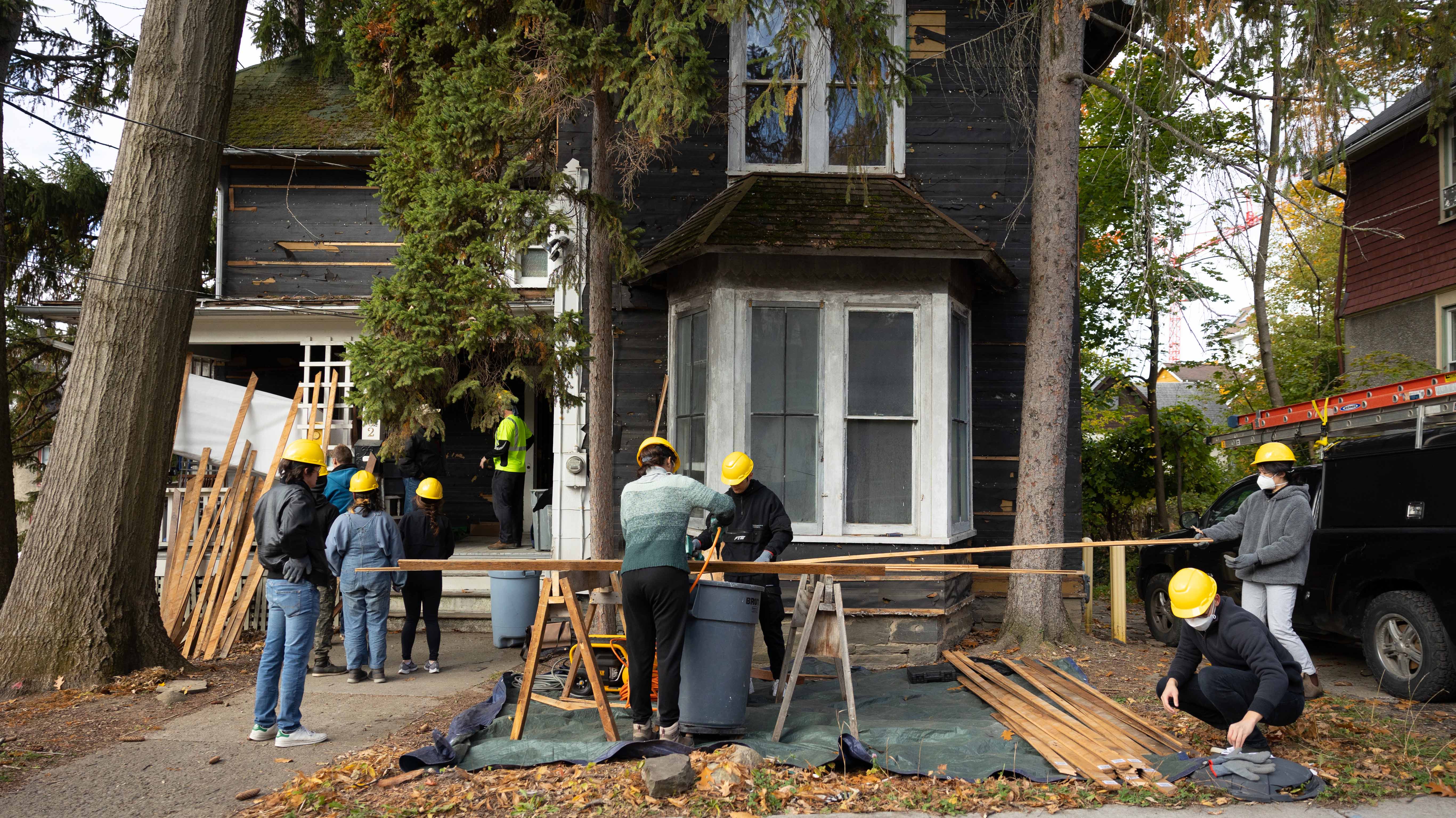 Construction workers wearing hard hats are renovating the exterior of a two-story house.