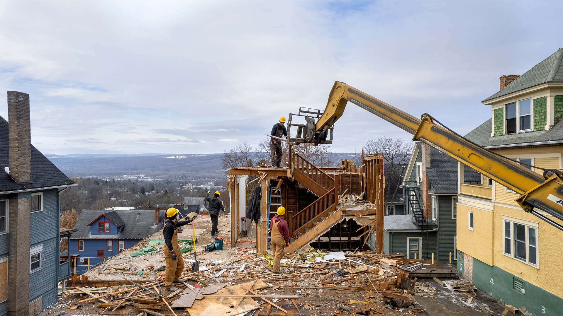 a construction crew deconstructing a house with a large yellow lift