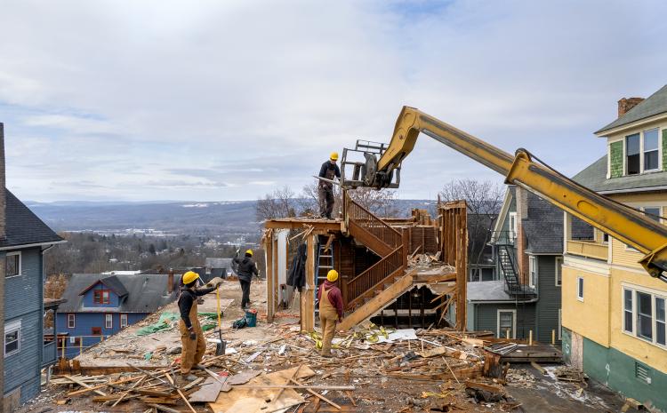 a construction crew deconstructing a house with a large yellow lift