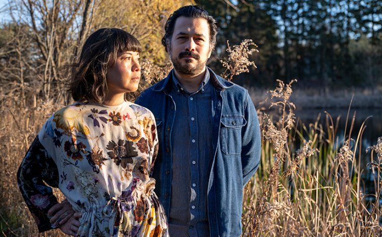 A man and woman standing in a wooded field at sunset