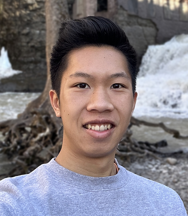 A man with black hair and a grey t-shirt smiles at the camera.