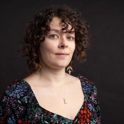 A person with curly hair and a floral dress in front of a dark background