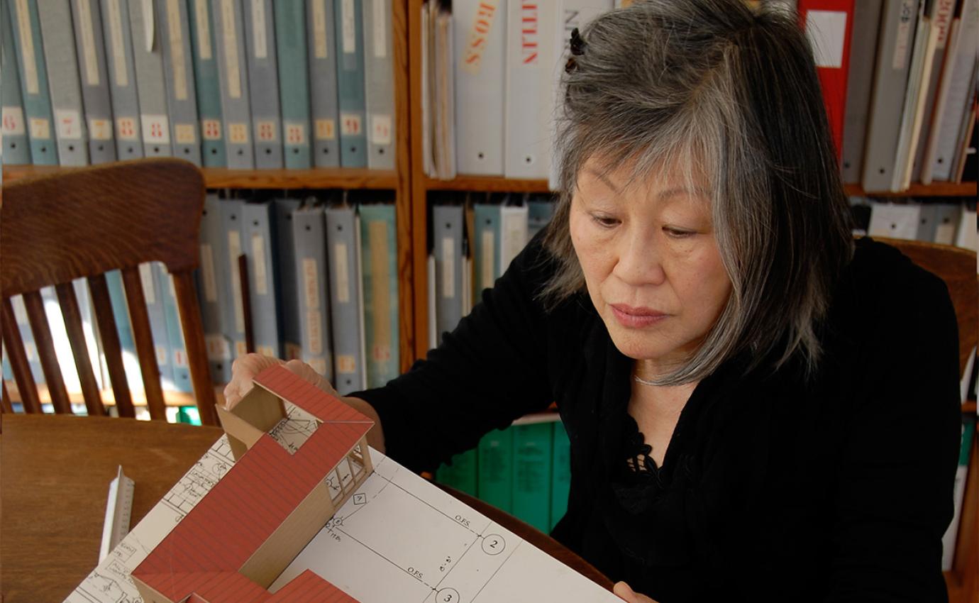 A person holding an architectural model and sitting in front of a book shelf.