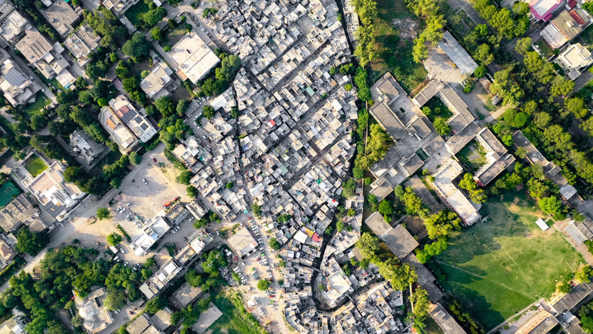 Aerial view of cluster of small houses surrounded by large concrete buildings and greenery