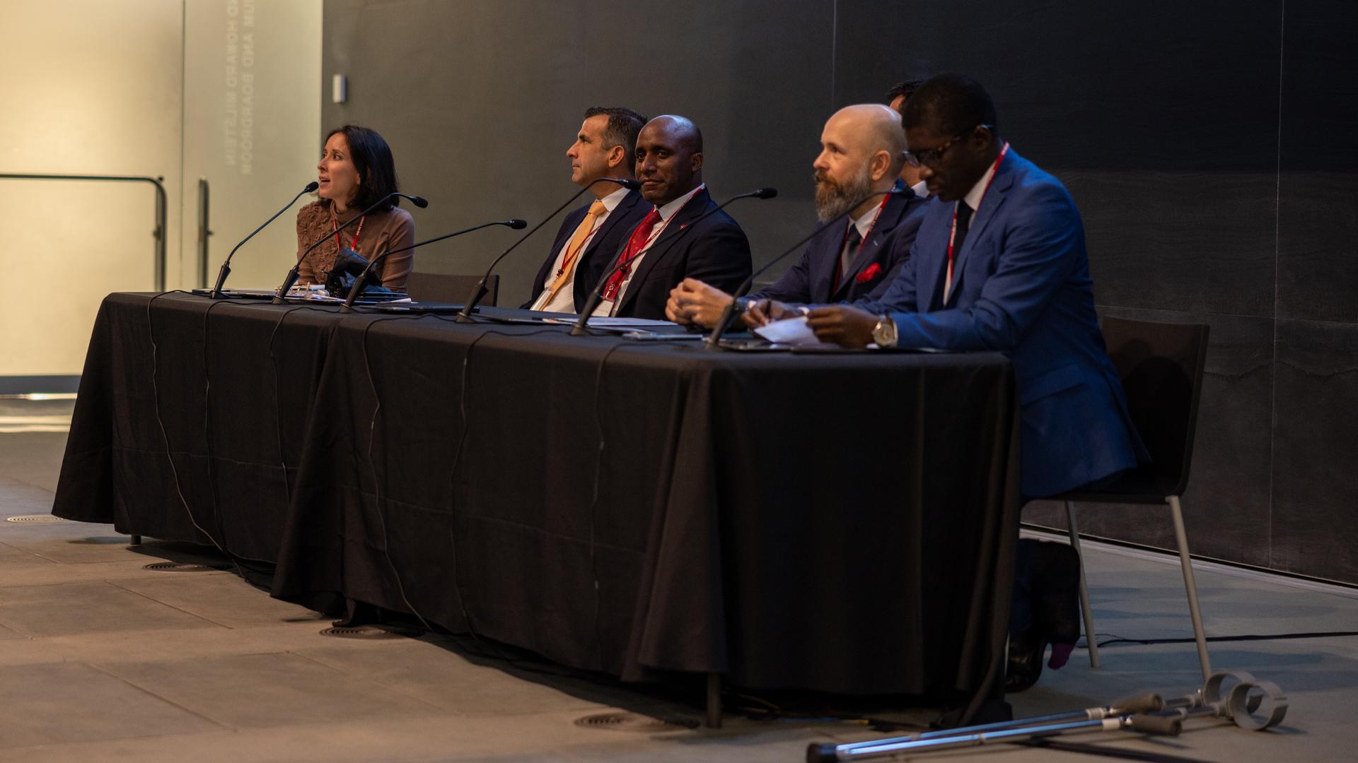 People sitting at a table with a black table cloth and microphones in front of them.